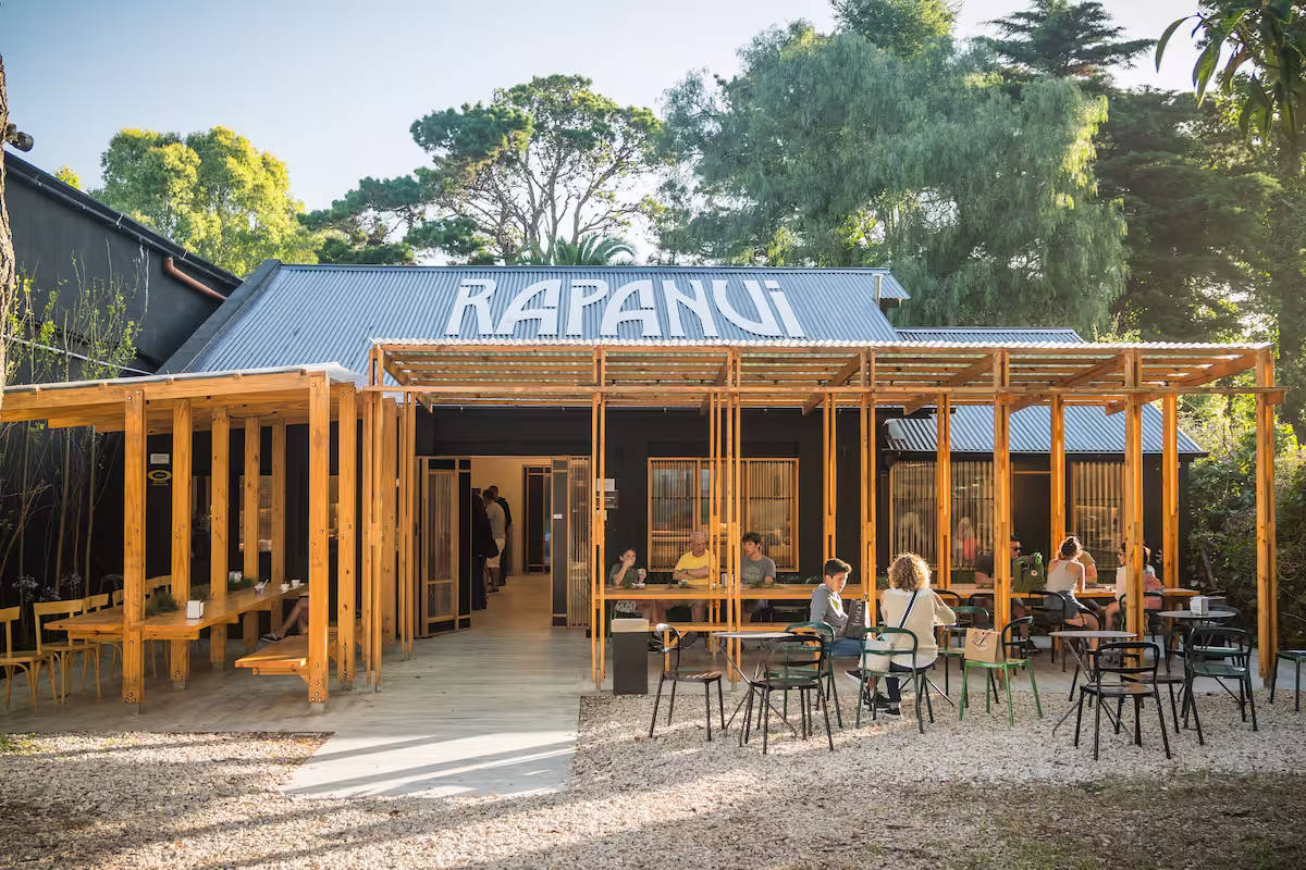 Fachada de Rapanui Pinamar, con pérgola de madera y mesas entre los pinos